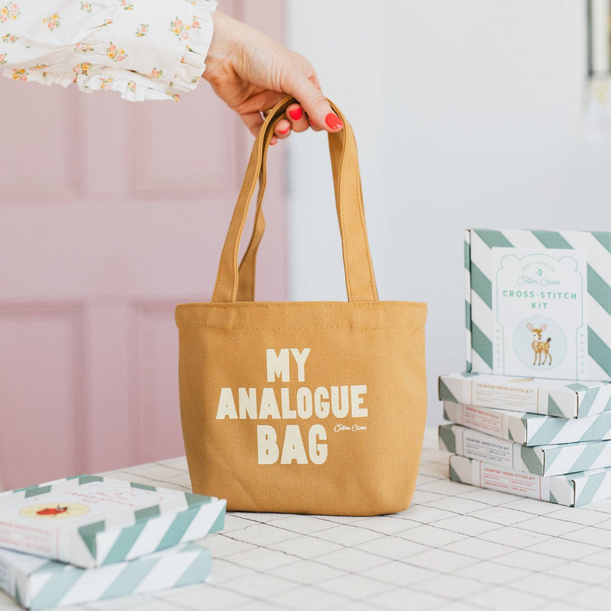 Brown tote bag with 'My Analogue Bag' text held by a hand on a light wooden surface.