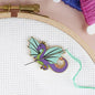 Embroidery hoop with a dragon-shaped needle minder on cross-stitched fabric.