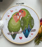 Cross-stitched parrot design in an embroidery hoop on a white background