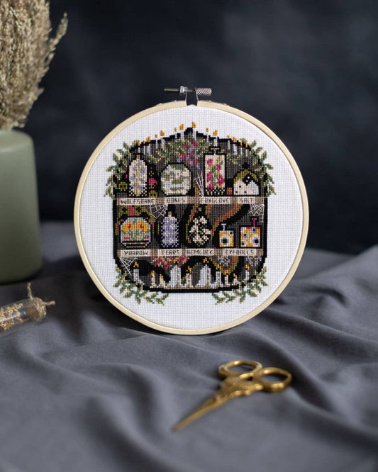The Apothecary Cross Stitch Kit by Innocent Bones. Embroidery hoop with decorative cross-stitch design on a dark fabric background