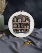 The Apothecary Cross Stitch Kit by Innocent Bones. Embroidery hoop with decorative cross-stitch design on a dark fabric background