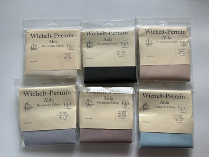 Six packaged fabric bolts from Wichelt-Permin Aida Premium Fabric arranged in a 2x3 grid on a white background. The fabrics shown are in beige, black, taupe, light blue, dusty rose, and navy colors.