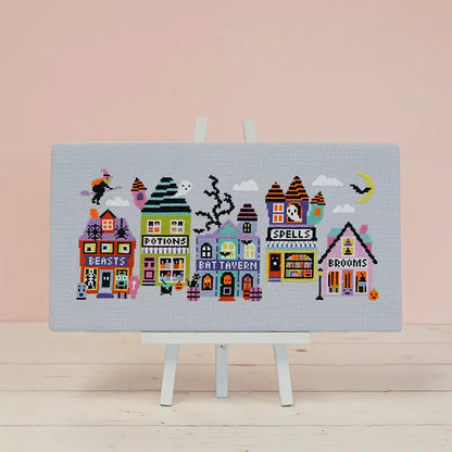 Cross-stitched design of colorful buildings on a light blue fabric with a pink background