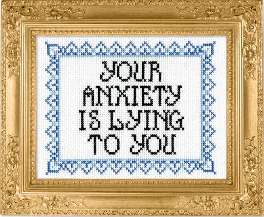 Decorative cross-stitch with 'Your anxiety is lying to you' text in a gold frame.