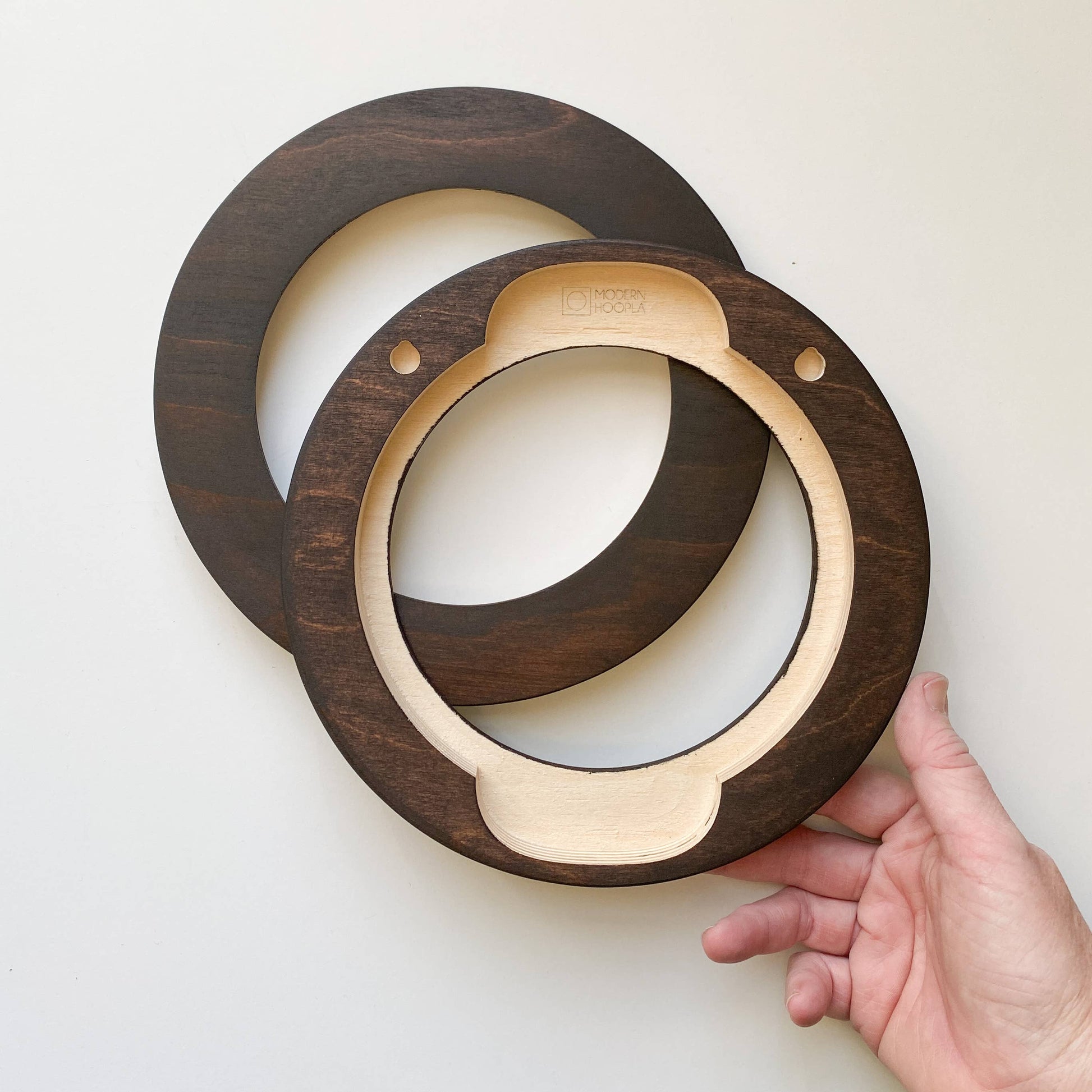 Wooden circular embroidery frame with a hand holding one of them on a light background